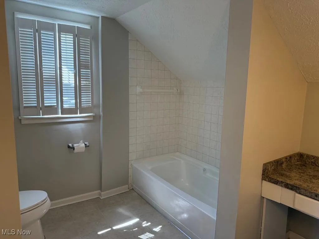 Full bath with a textured ceiling, lofted ceiling, tile patterned floors, and vanity