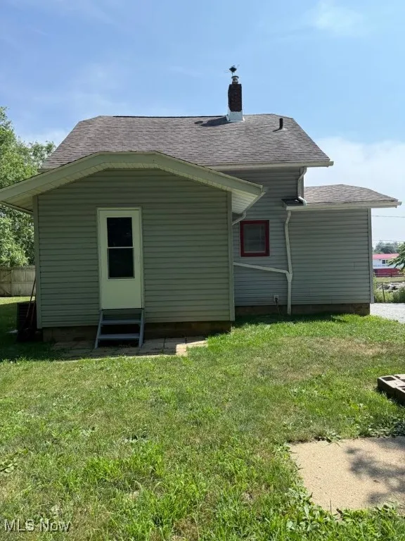 Rear view of property featuring a shingled roof, entry steps, a yard, and a chimney
