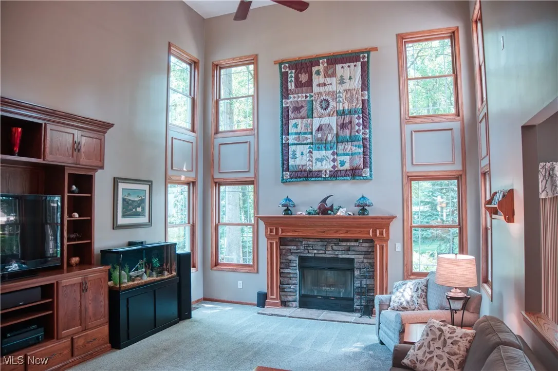 Carpeted living area featuring a ceiling fan, a high ceiling, and a fireplace