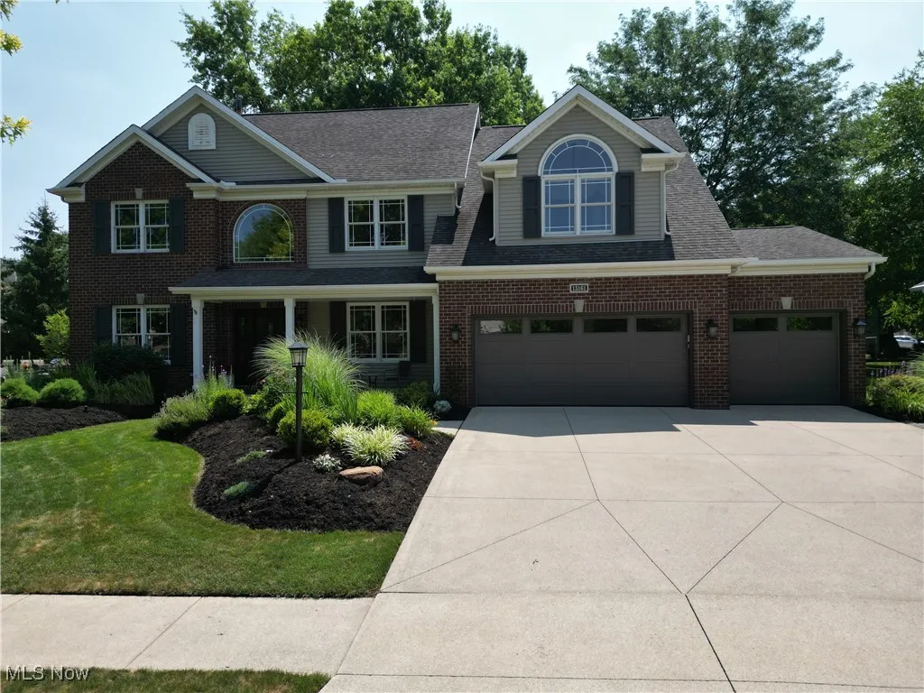 Traditional home with concrete driveway, a garage, brick siding, a front lawn, and a shingled roof