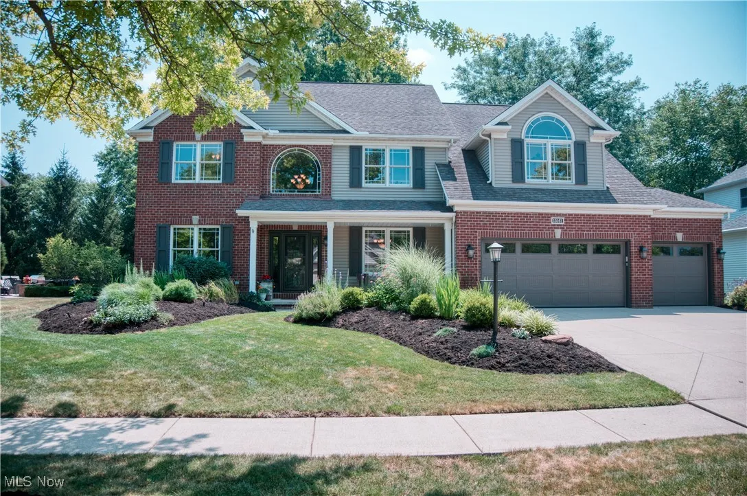 Traditional-style home with driveway, a front lawn, roof with shingles, a porch, and brick siding