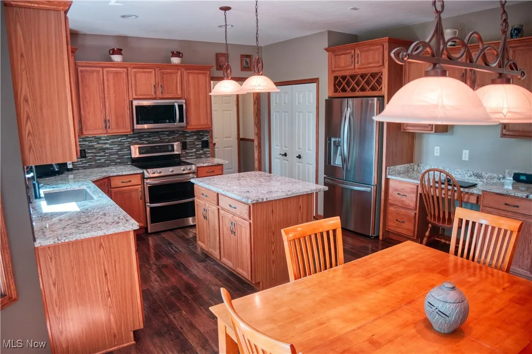 Kitchen featuring stainless steel appliances, backsplash, a kitchen island, dark wood-style flooring, and decorative light fixtures