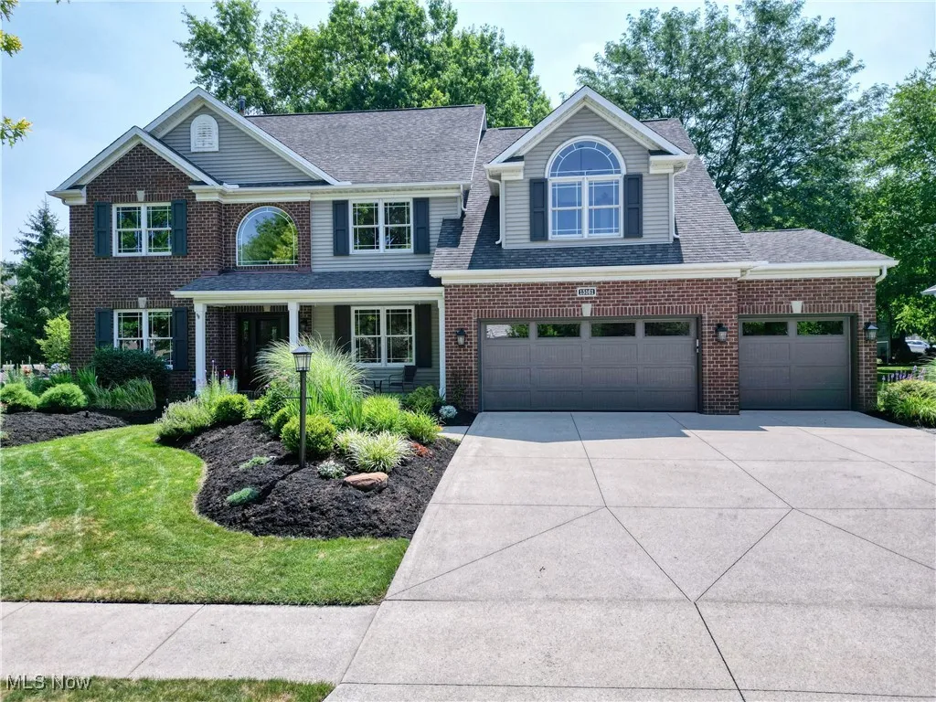 Traditional-style home featuring driveway, roof with shingles, brick siding, an attached garage, and a front yard