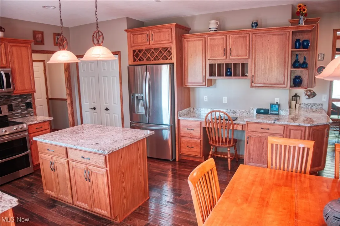 Kitchen with appliances with stainless steel finishes, open shelves, dark wood finished floors, hanging light fixtures, and light stone counters