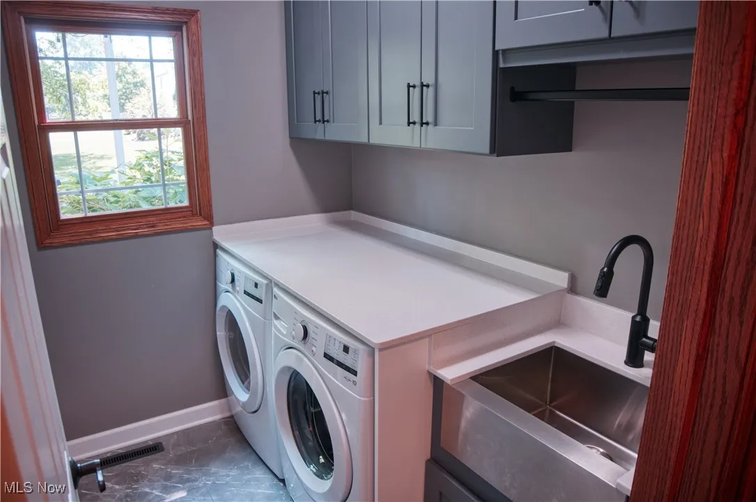 Laundry area featuring washing machine and clothes dryer, cabinet space, and dark marble finish floors