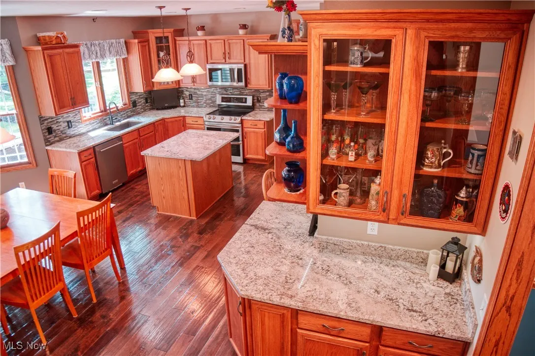 Kitchen featuring stainless steel appliances, a center island, tasteful backsplash, dark wood-style floors, and glass insert cabinets