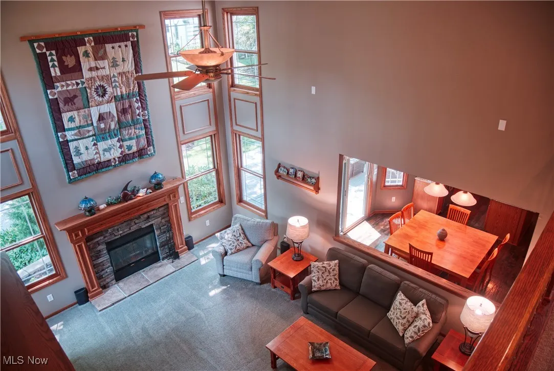 Carpeted living room with a stone fireplace, a towering ceiling, and a ceiling fan