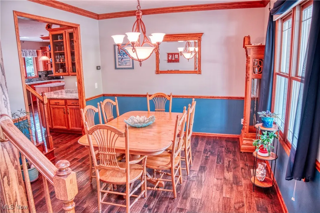 Dining space with dark wood-style floors, ornamental molding, and a chandelier