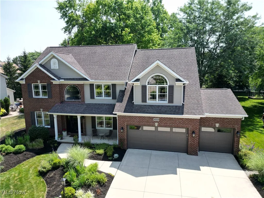 Traditional-style house featuring a porch, concrete driveway, roof with shingles, and brick siding