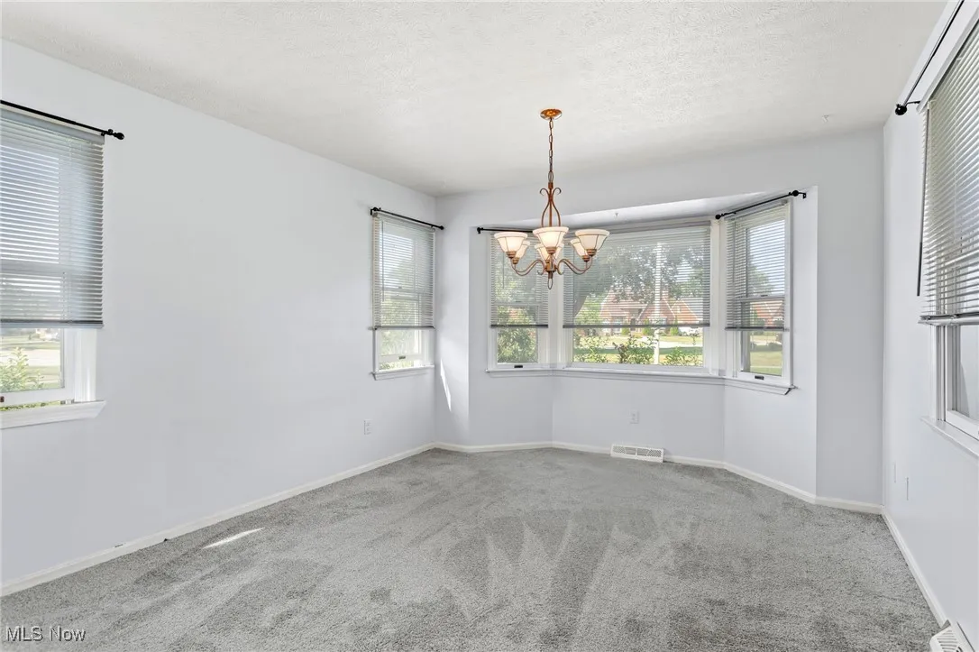 Unfurnished room with a chandelier, carpet, and a textured ceiling