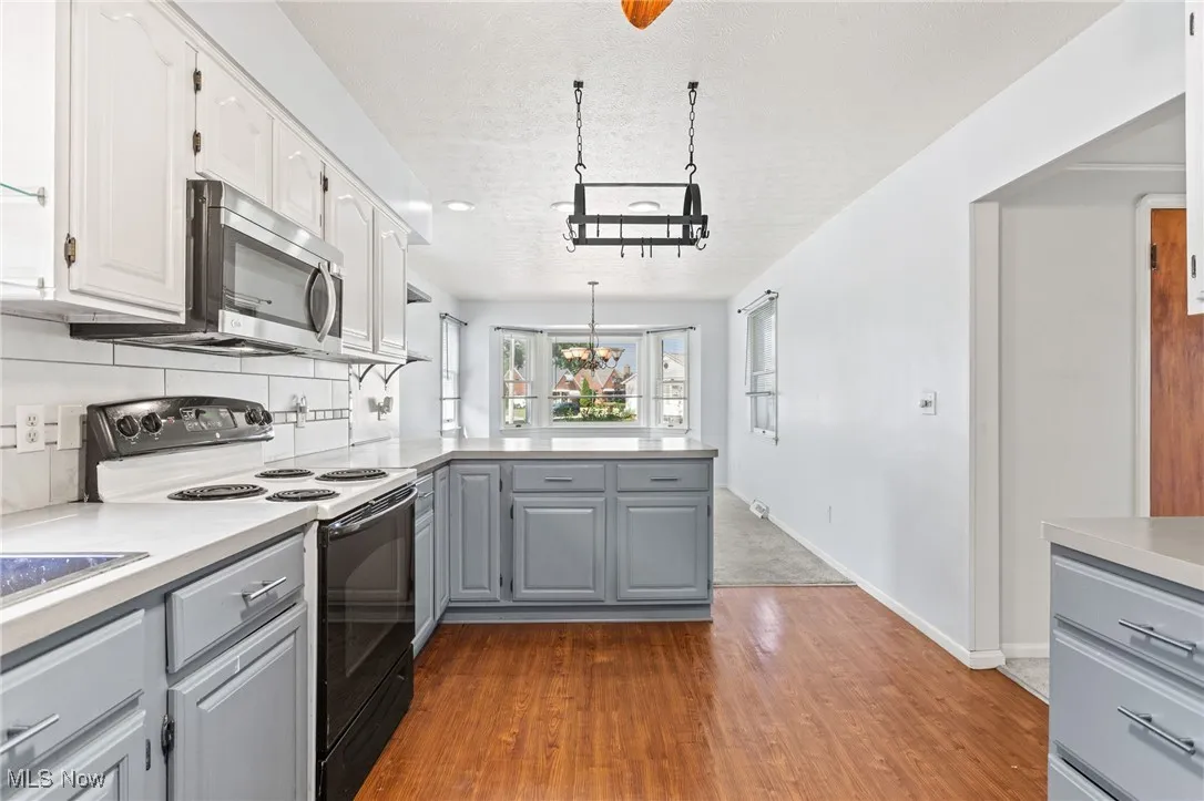 Kitchen with gray cabinets, electric range, a peninsula, stainless steel microwave, and a textured ceiling