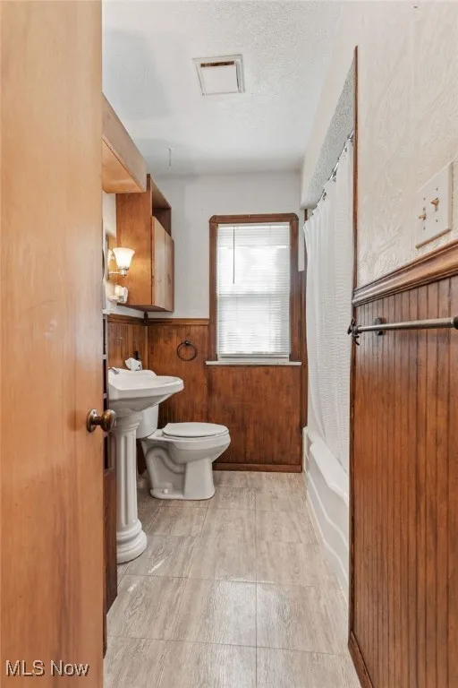 Full bathroom featuring a wainscoted wall, a textured ceiling, and shower / bath combination with curtain