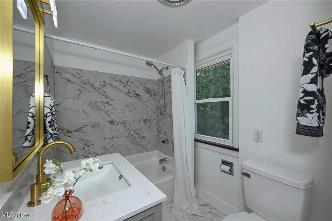 Full bathroom featuring vanity, shower / tub combo with curtain, and marble look tiles