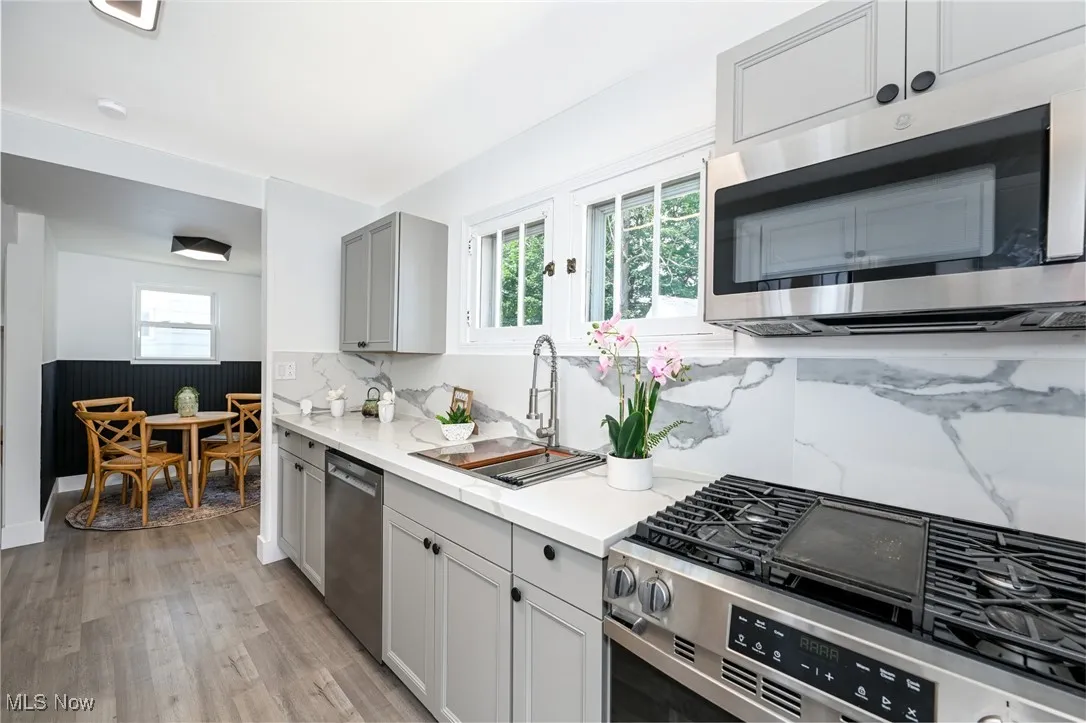 Kitchen featuring stainless steel appliances, light wood finished floors, decorative backsplash, gray cabinetry, and light stone countertops