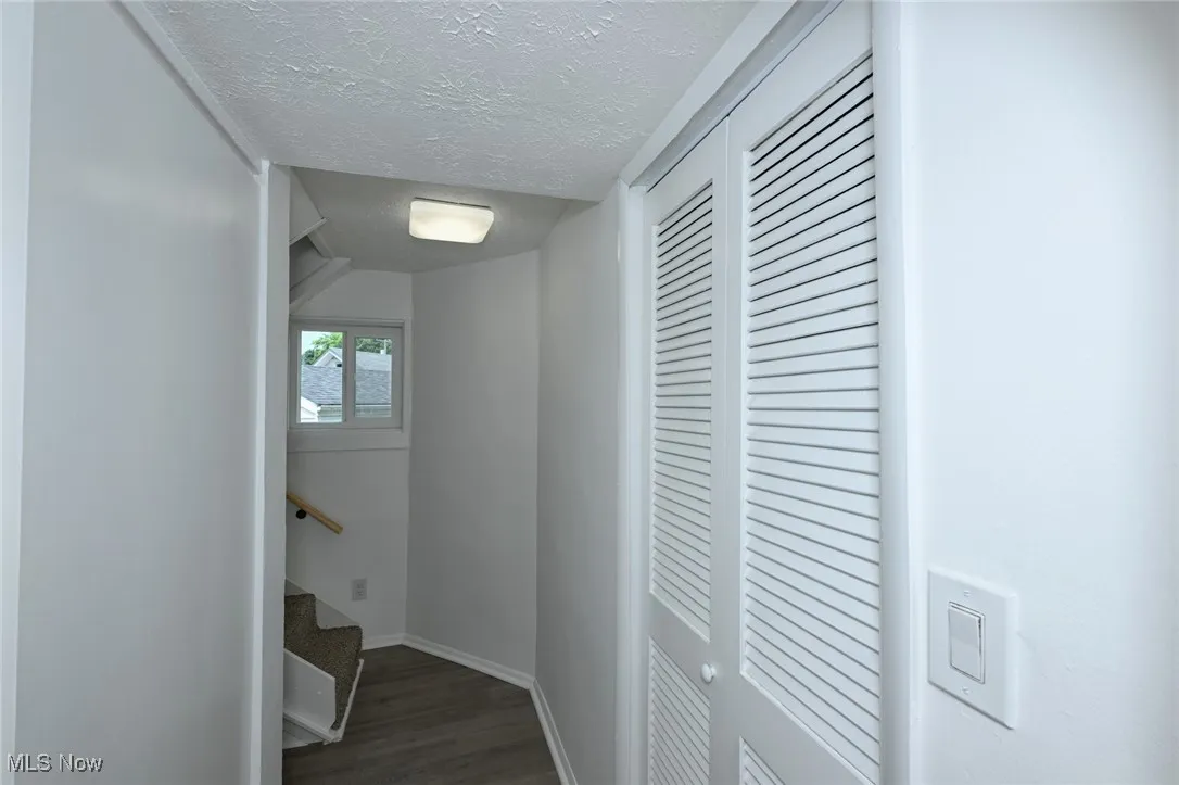 Corridor featuring a textured ceiling, wood finished floors, and stairs