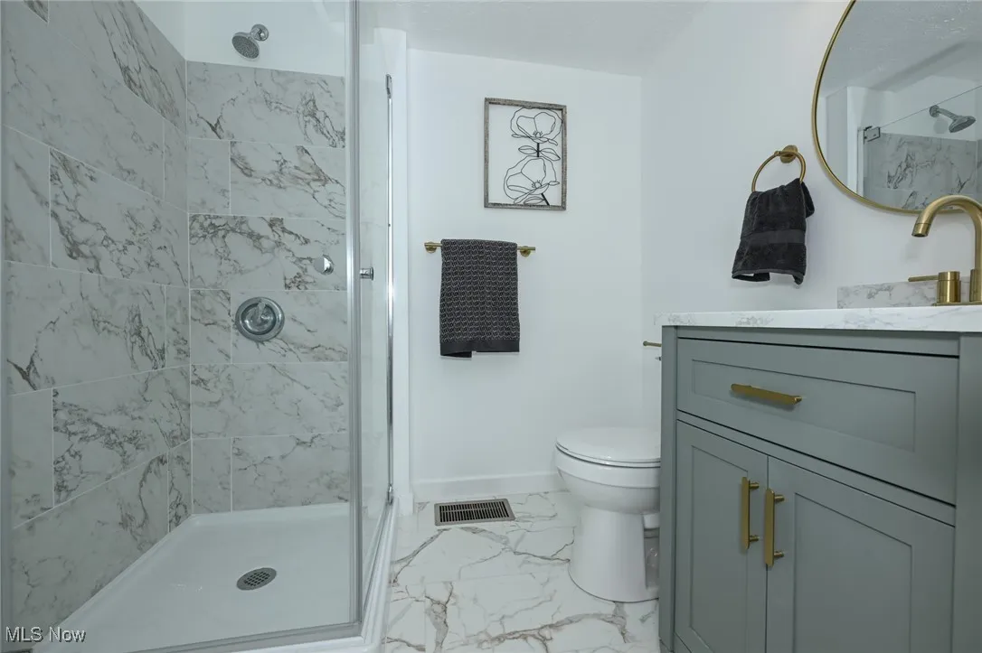 Full bath featuring marble look tiles, vanity, and a shower stall