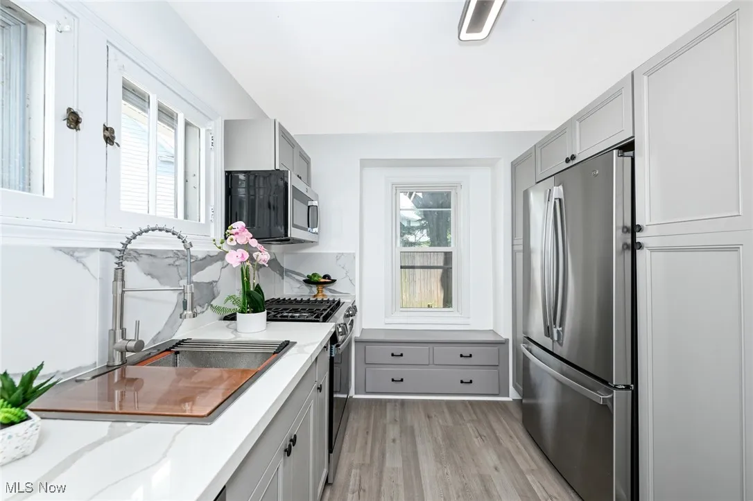Kitchen featuring appliances with stainless steel finishes, gray cabinets, light wood finished floors, and light stone countertops