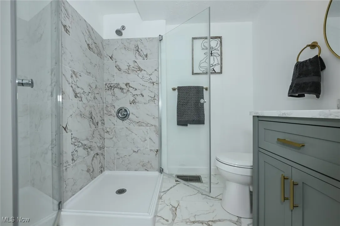 Full bathroom with marble look tiles, a stall shower, and vanity