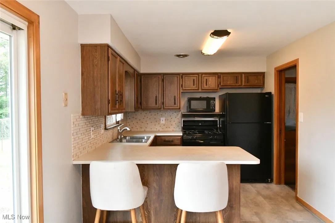 Kitchen featuring black appliances, light countertops, backsplash, and a peninsula