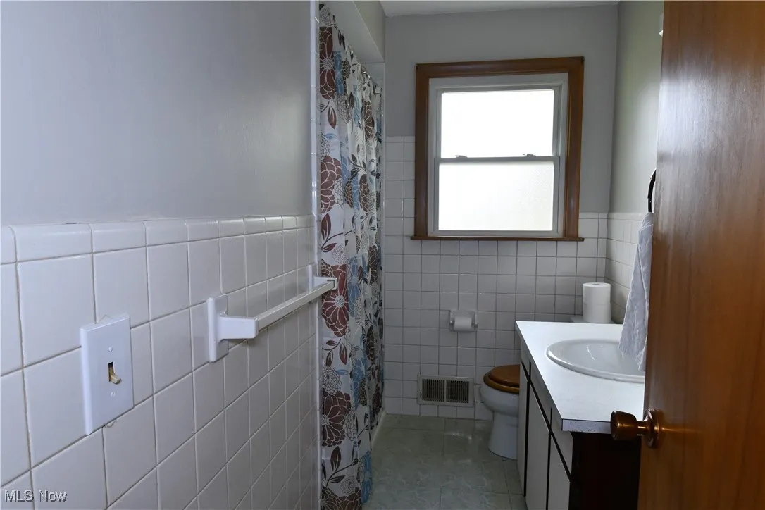 Full bathroom with tile walls, vanity, tile patterned flooring, wainscoting, and curtained shower