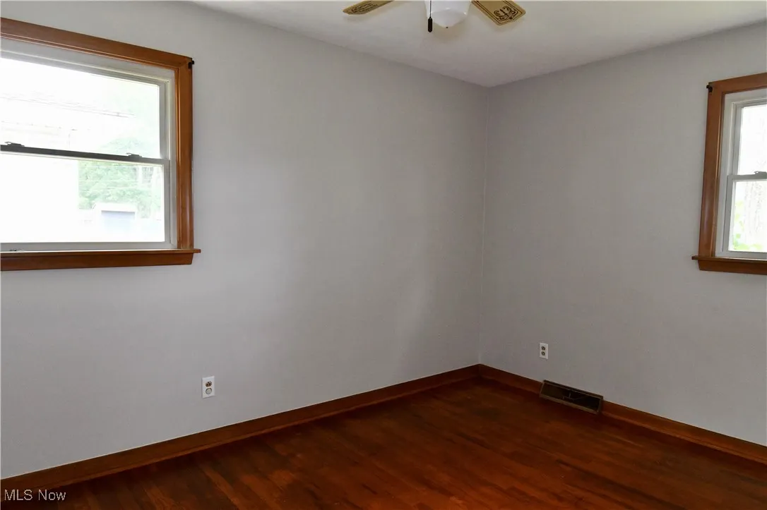 Unfurnished room featuring dark wood-style flooring and ceiling fan