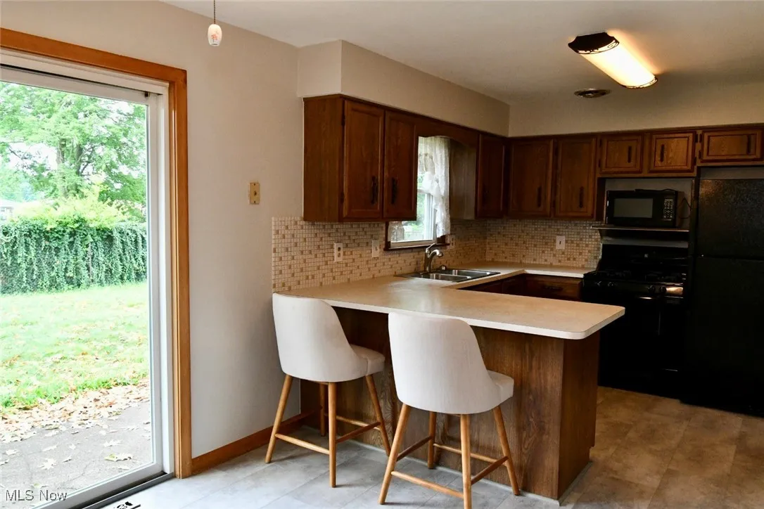 Kitchen with black appliances, decorative backsplash, light countertops, a peninsula, and a breakfast bar area