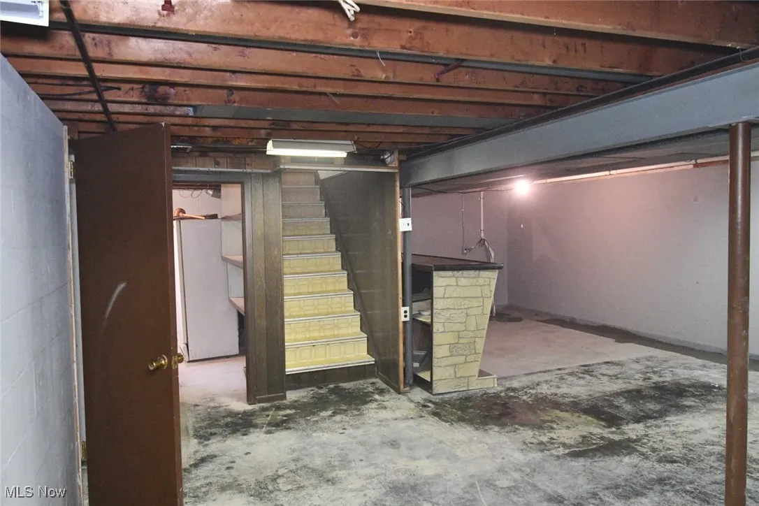 Unfinished basement featuring stairs and freestanding refrigerator