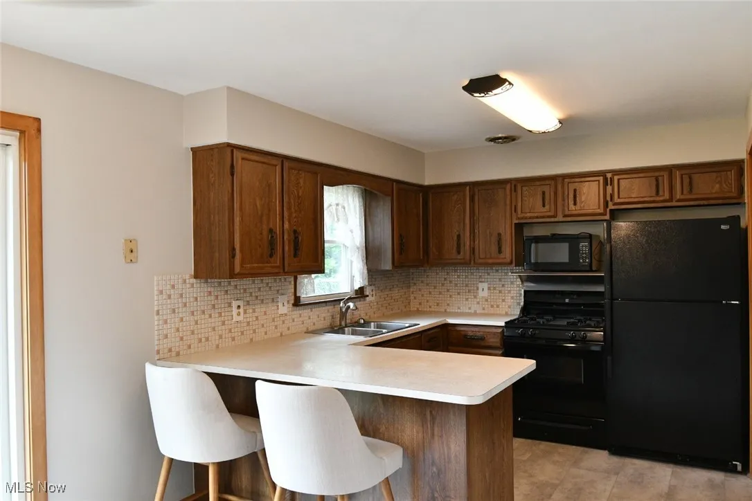 Kitchen featuring black appliances, a peninsula, light countertops, backsplash, and a kitchen bar