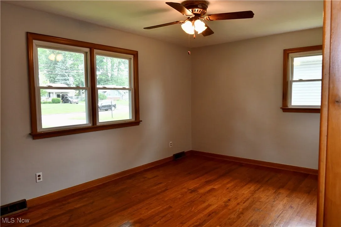 Empty room with plenty of natural light, wood finished floors, and a ceiling fan