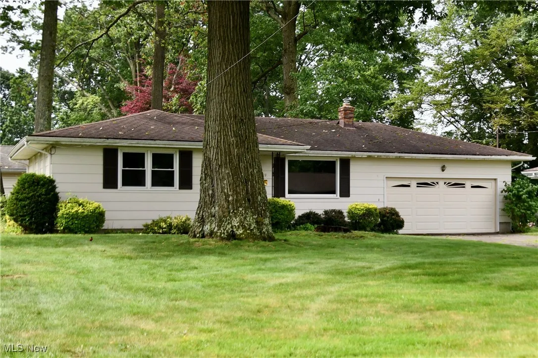 Single story home featuring a chimney, an attached garage, a front lawn, and driveway