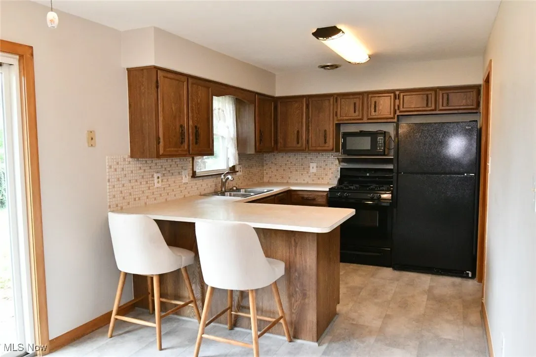 Kitchen featuring black appliances, a peninsula, backsplash, light countertops, and brown cabinets