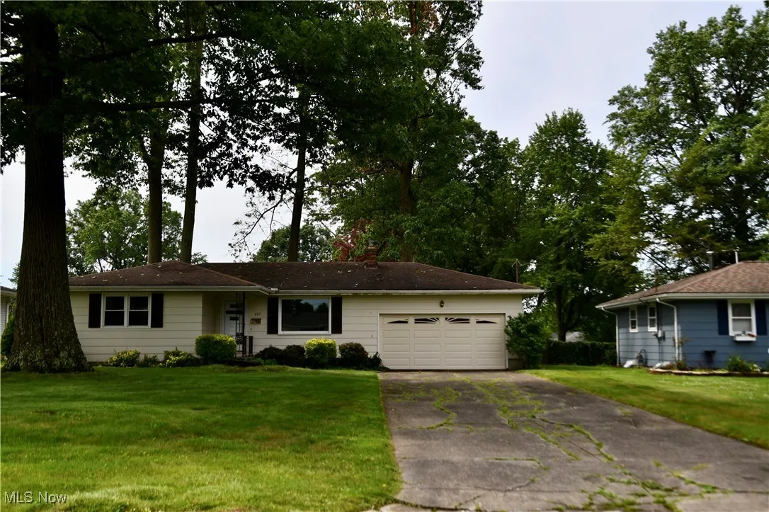 Ranch-style home with a garage, asphalt driveway, a front lawn, and a chimney