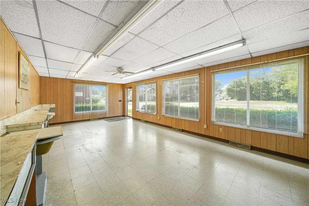 Unfurnished living room with light floors, wooden walls, a drop ceiling, and ceiling fan
