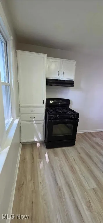 Kitchen view of gas stove, light lvt floors, white cabinets, and under cabinet range hood