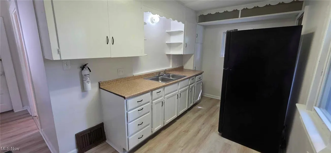 Kitchen featuring freestanding refrigerator, light lvt floors, white cabinetry, open shelves, and light countertops