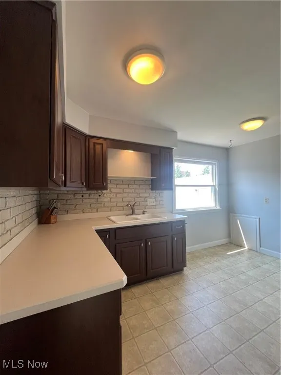 Kitchen featuring decorative backsplash, dark brown cabinets, open shelves, light countertops, and light tile patterned floors
