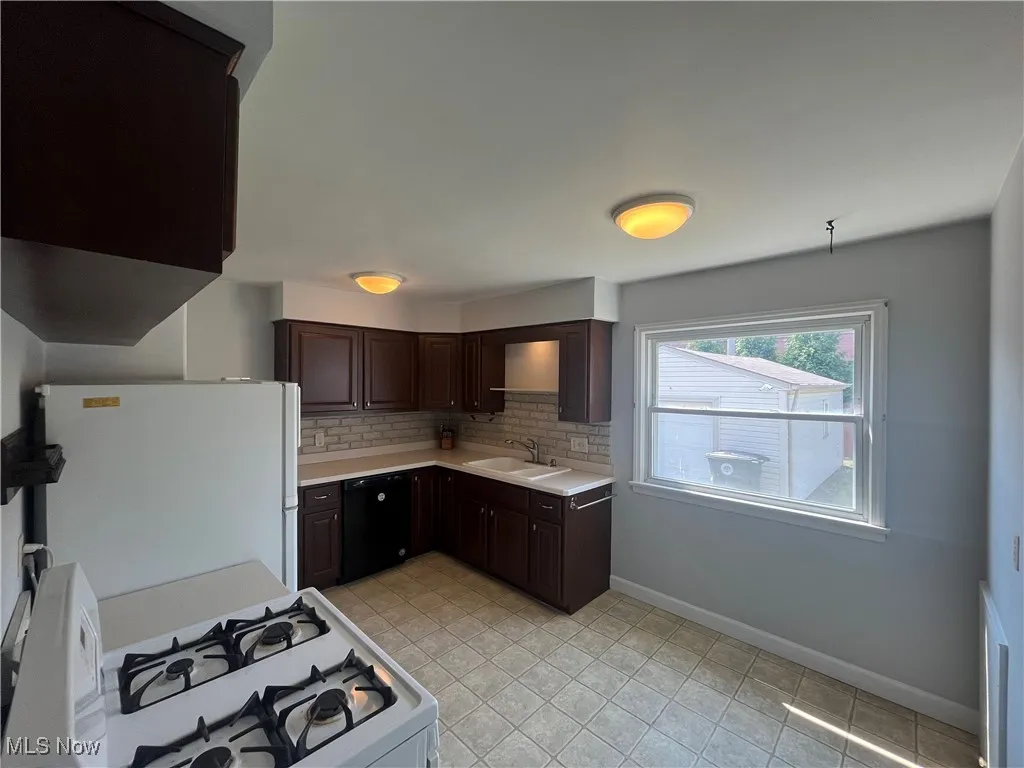 Kitchen featuring light countertops, white appliances, and dark brown cabinetry