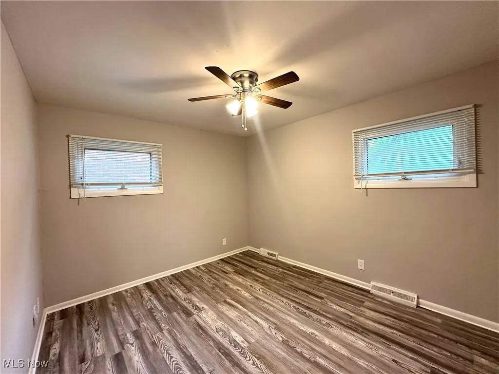 Empty room featuring plenty of natural light, dark wood-style flooring, and ceiling fan