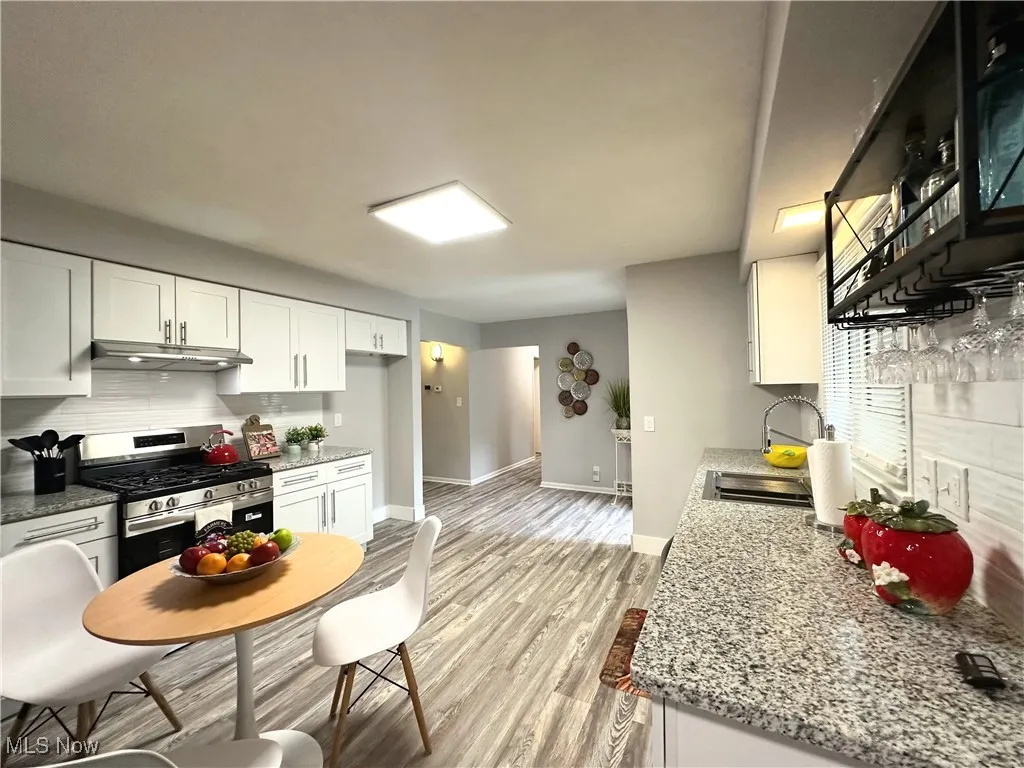 Kitchen featuring stainless steel gas stove, tasteful backsplash, white cabinets, light wood-type flooring, and under cabinet range hood