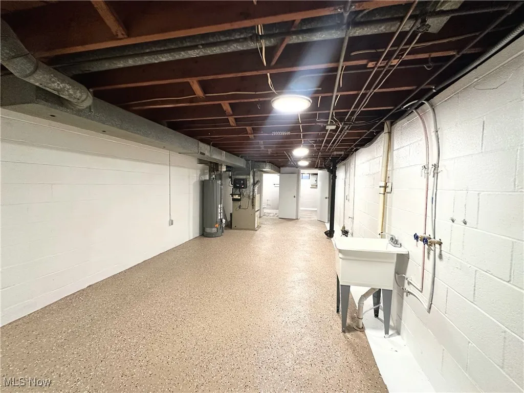 Unfinished below grade area featuring concrete block wall, gas water heater, and heating unit