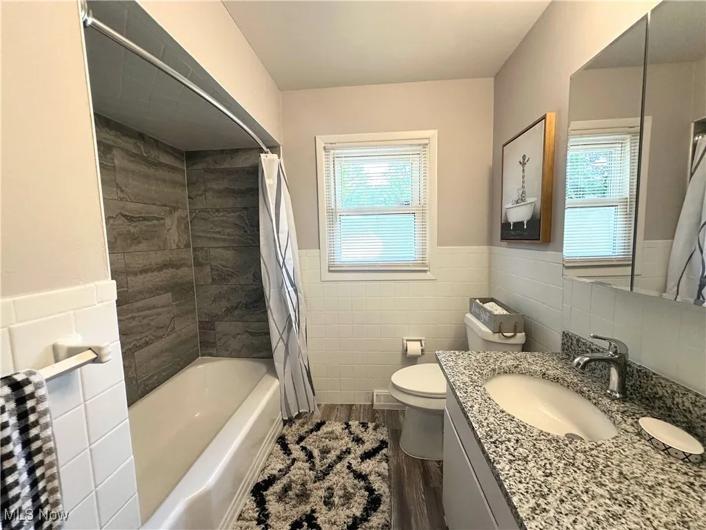 Bathroom with vanity, tile walls, wood finished floors, a wainscoted wall, and shower / bathtub combination with curtain