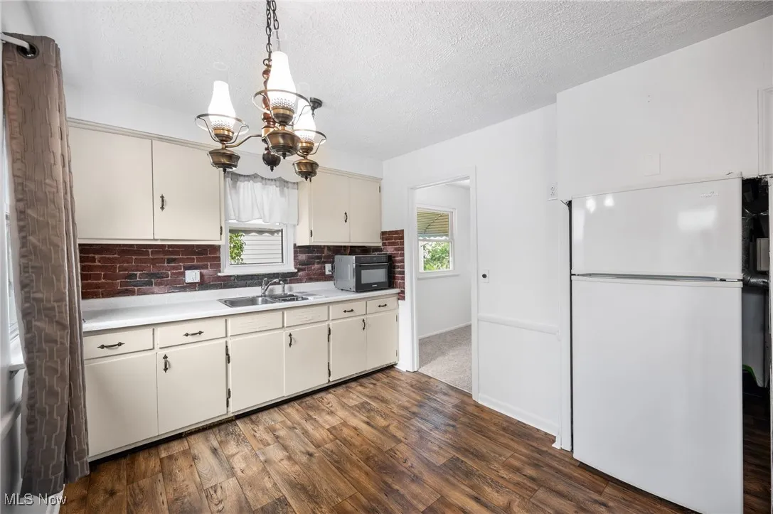 Kitchen with freestanding refrigerator, light countertops, wood-style floors, a chandelier, and tasteful backsplash