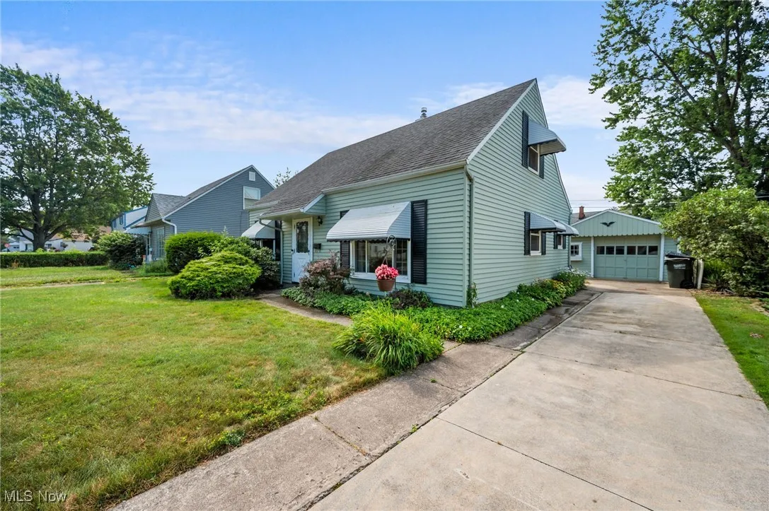 View of front of home featuring an outdoor structure, a front yard, a garage, concrete driveway, and a shingled roof