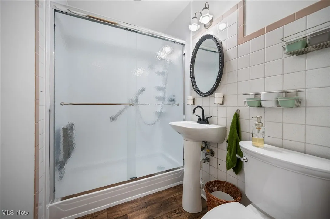 Full bath with a stall shower, wood style floors, and tile walls