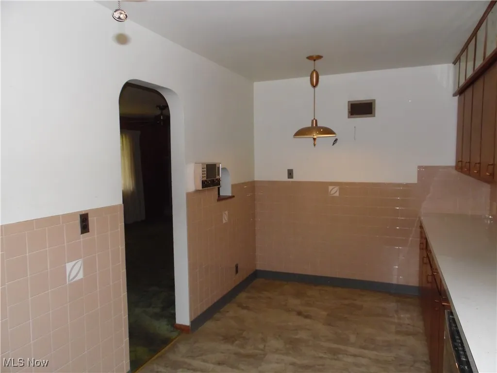 Kitchen featuring tile walls, arched walkways, a wainscoted wall, decorative light fixtures, and a peninsula