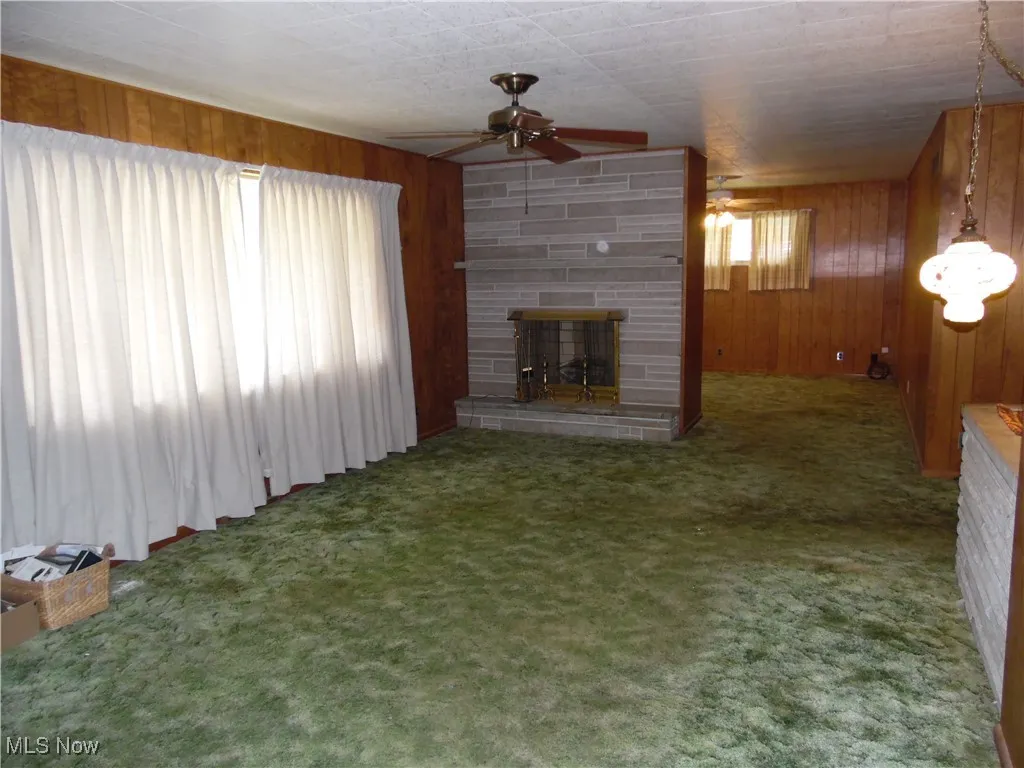 Unfurnished living room featuring a fireplace, wood walls, ceiling fan, and carpet flooring
