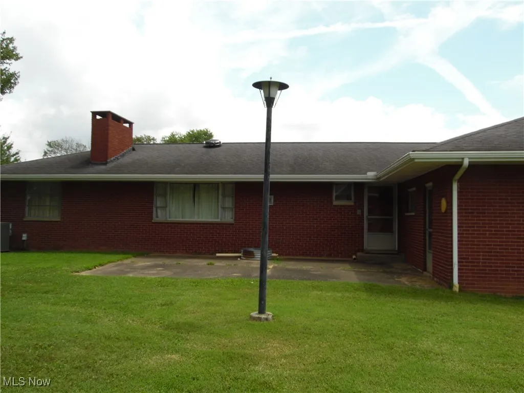 Rear view of property featuring a patio area, brick siding, a chimney, and a yard
