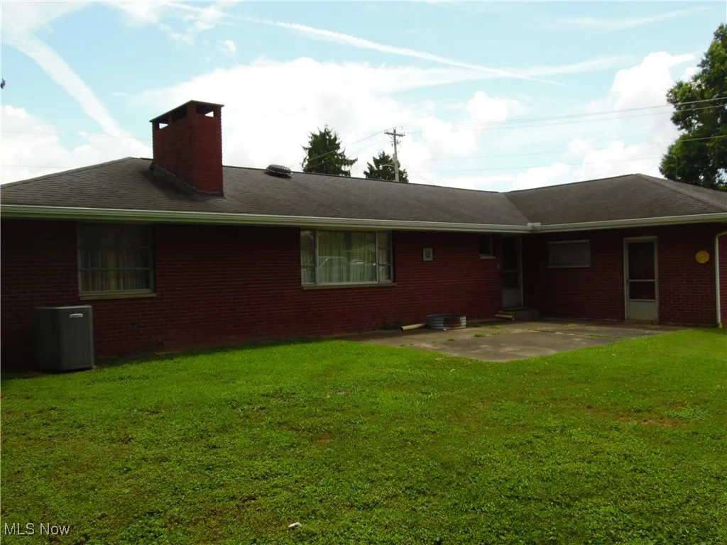 Rear view of house featuring a chimney, a patio area, a yard, and brick siding