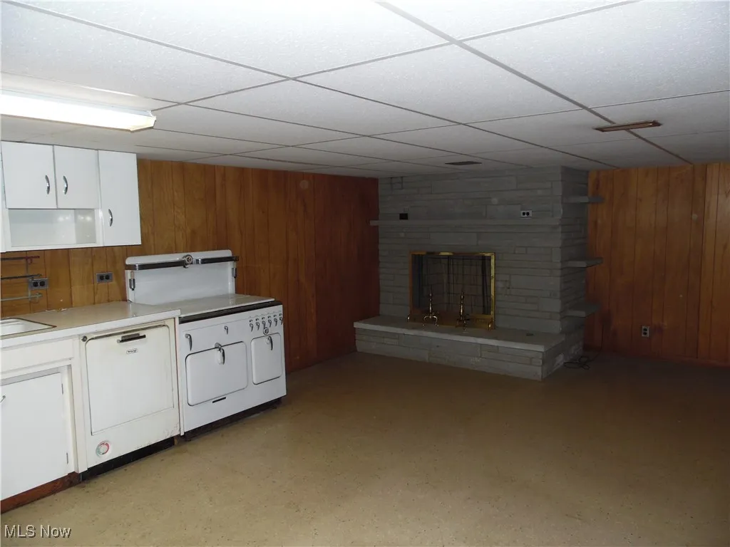 Kitchen with wood walls, white cabinetry, a fireplace, a drop ceiling, and light countertops