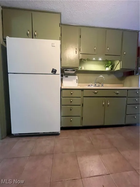 Kitchen featuring green cabinets, fridge, open shelves, a textured ceiling, and light tile patterned flooring